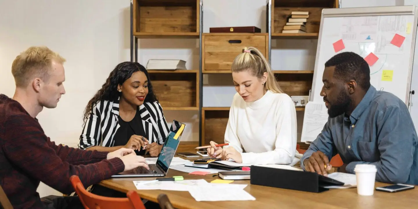 Diverse team of creative professionals collaborating around a meeting table, discussing leadership and business strategies for a design startup.