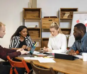 Diverse team of creative professionals collaborating around a meeting table, discussing leadership and business strategies for a design startup.