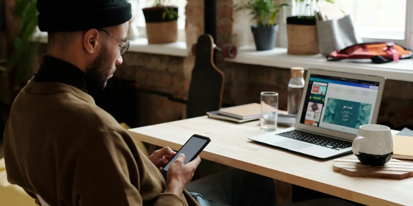 Design entrepreneur reviewing growth strategies on a smartphone and laptop in a modern workspace, representing a startup roadmap for creative business development.