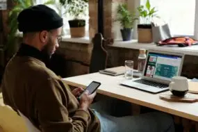 Design entrepreneur reviewing growth strategies on a smartphone and laptop in a modern workspace, representing a startup roadmap for creative business development.
