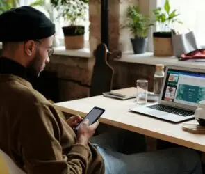 Design entrepreneur reviewing growth strategies on a smartphone and laptop in a modern workspace, representing a startup roadmap for creative business development.