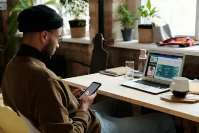 Design entrepreneur reviewing growth strategies on a smartphone and laptop in a modern workspace, representing a startup roadmap for creative business development.