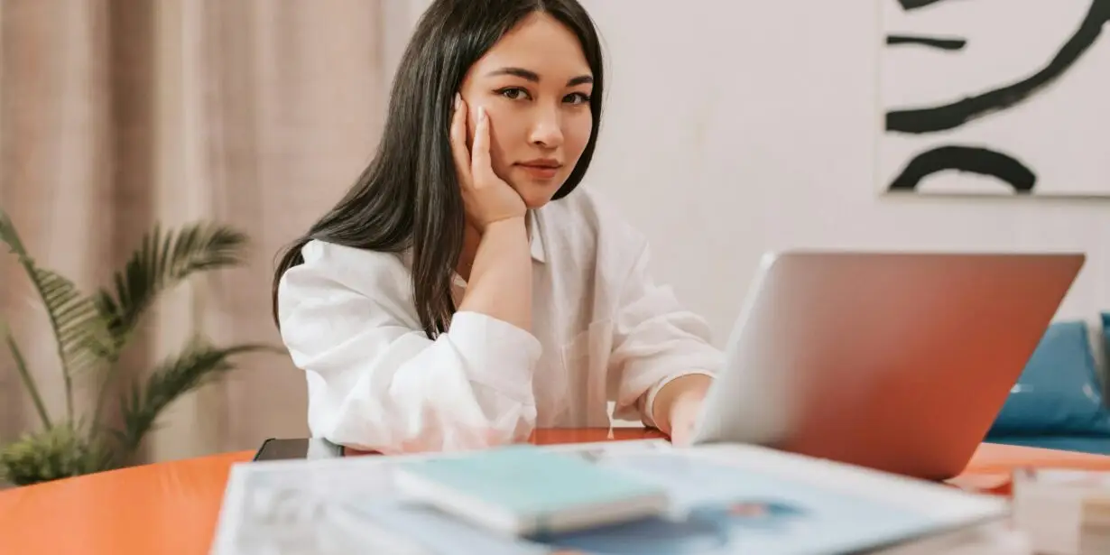 Freelance designer working on a proposal at a laptop with notebooks and reference materials on the desk.