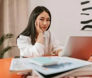 Freelance designer working on a proposal at a laptop with notebooks and reference materials on the desk.