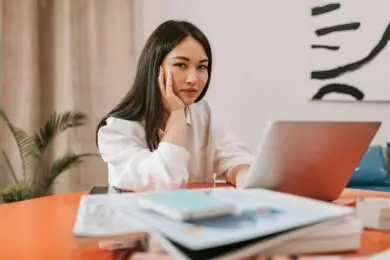 Freelance designer working on a proposal at a laptop with notebooks and reference materials on the desk.