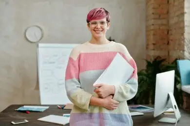 Confident freelance designer standing in a modern creative workspace, holding a notebook with design strategy plans, symbolizing business growth and scaling success.