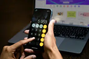 Person using smartphone calculator to determine pricing and profit margins for digital products.