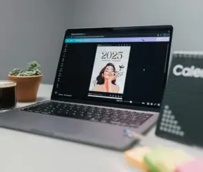 Laptop displaying a Canva-designed 2025 personal planner template on a desk with coffee, plant, and calendar board.