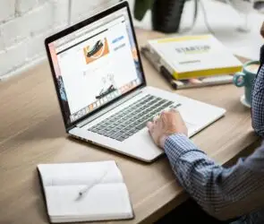 Designer managing an online digital product store on a laptop from a workspace desk.