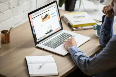 Designer managing an online digital product store on a laptop from a workspace desk.