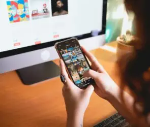 Design entrepreneur managing digital content and social media on smartphone while working at desktop computer.