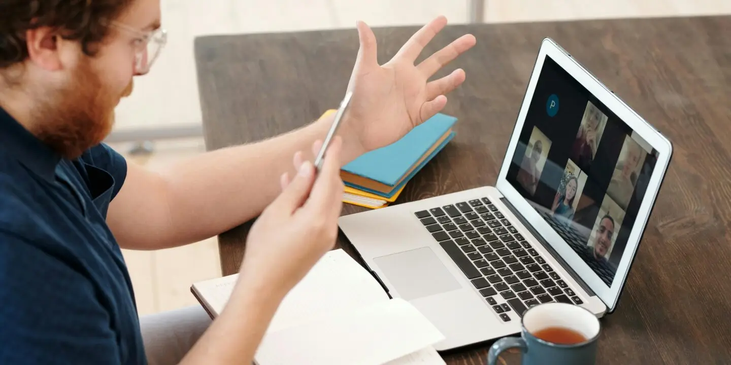 Designer participating in a video conference on a laptop while holding a smartphone at a desk.