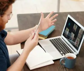 Designer participating in a video conference on a laptop while holding a smartphone at a desk.