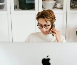 Woman talking on phone while working behind a desktop computer in a home office.