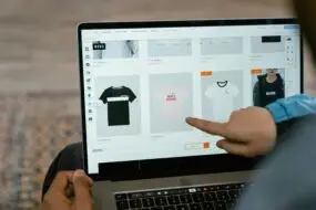 Person browsing custom t-shirt products on an online store using a laptop.