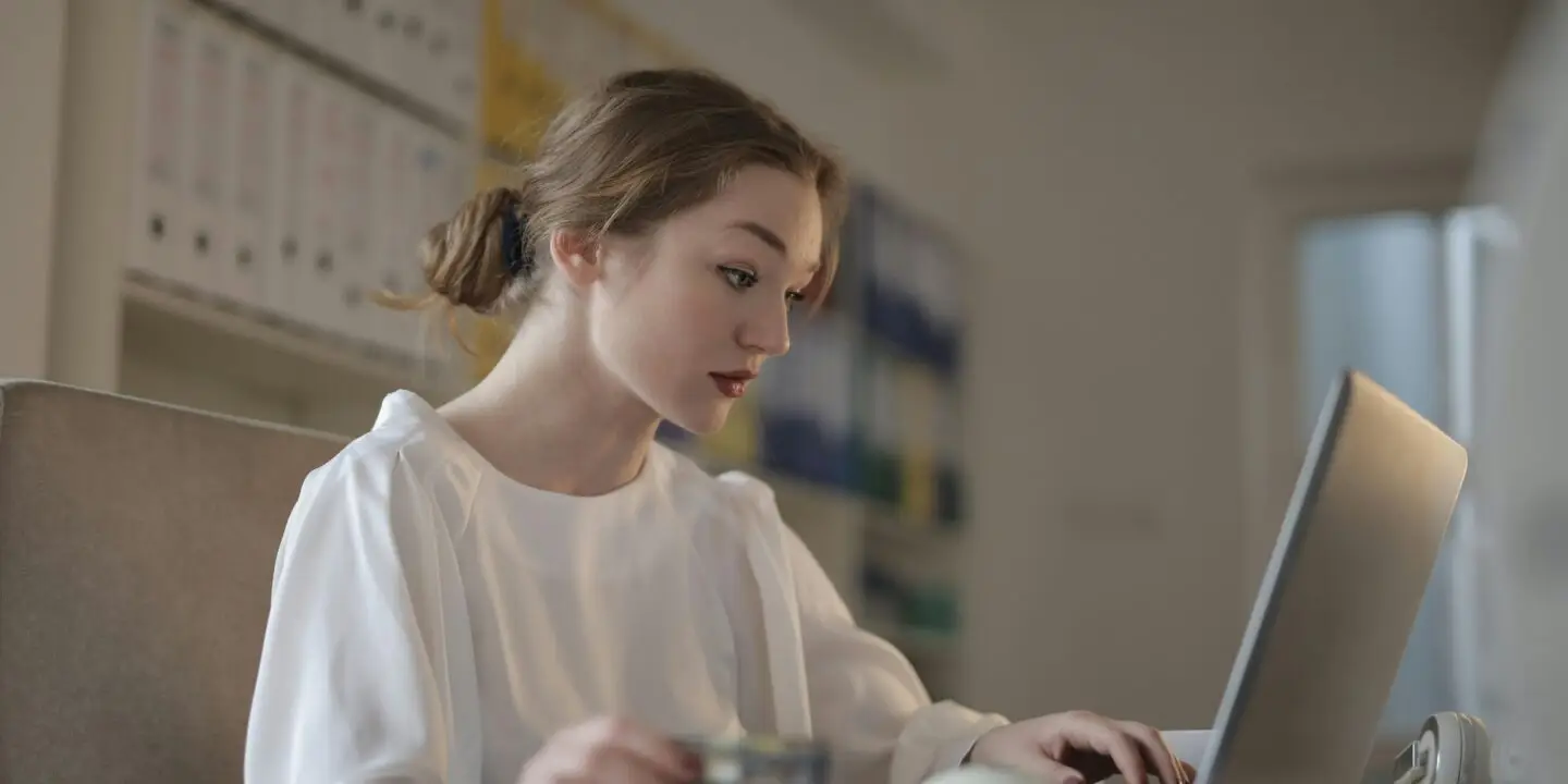 Woman working on laptop at desk while holding a payment card in a home office.