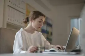 Woman working on laptop at desk while holding a payment card in a home office.