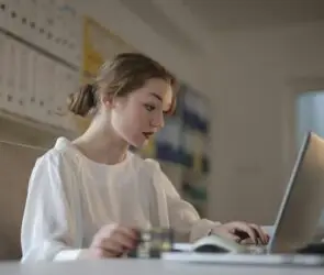 Woman working on laptop at desk while holding a payment card in a home office.