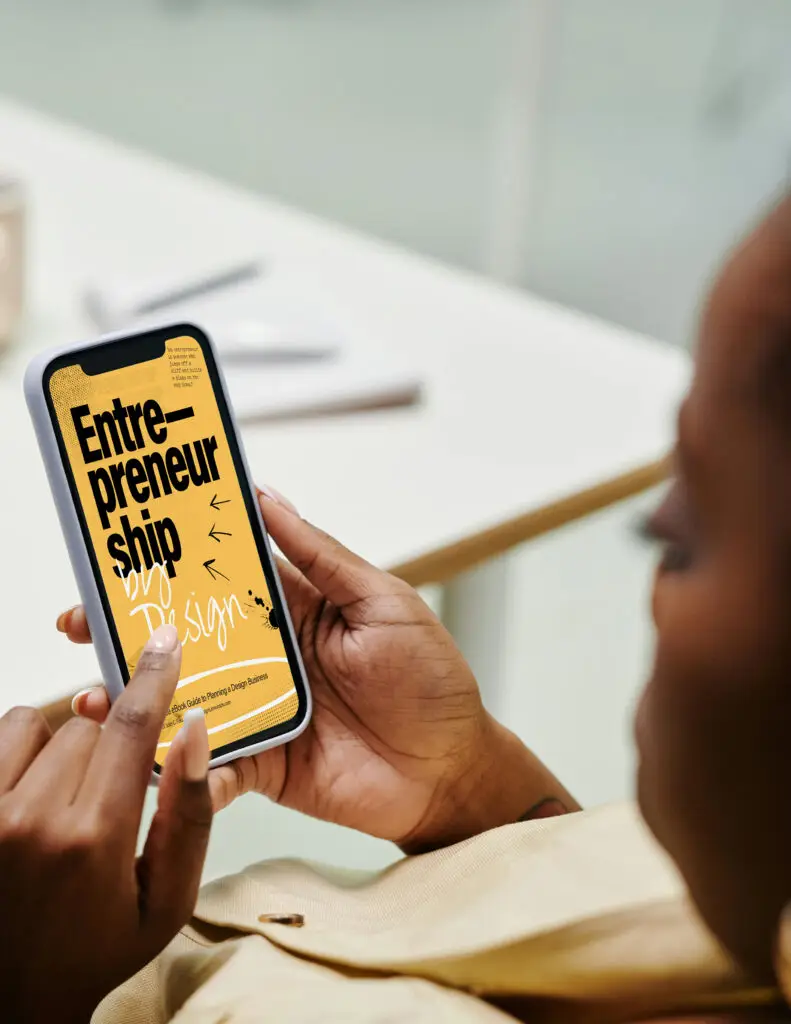 Person holding a smartphone displaying the “Entrepreneurship by Design” digital guide cover on screen.