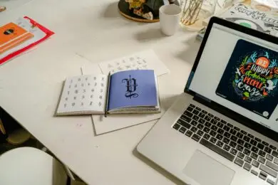 Designer workspace featuring typography references, lettering designs, and a laptop displaying digital artwork creation.