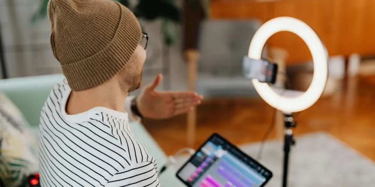 Content creator filming videos with a smartphone and ring light while reviewing digital content on a tablet.
