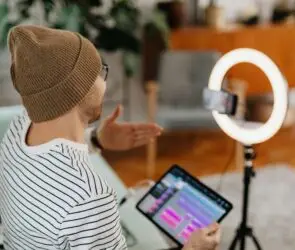 Content creator filming videos with a smartphone and ring light while reviewing digital content on a tablet.