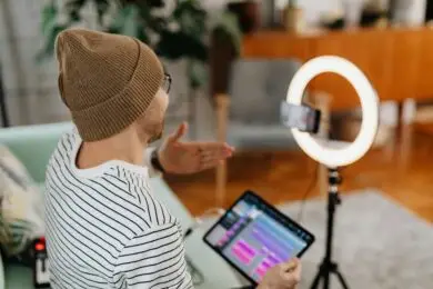 Content creator filming videos with a smartphone and ring light while reviewing digital content on a tablet.