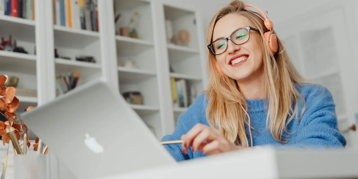 Designer smiling while working on a laptop with headphones in a home office.