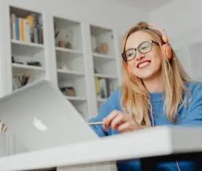 Designer smiling while working on a laptop with headphones in a home office.