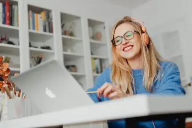 Designer smiling while working on a laptop with headphones in a home office.