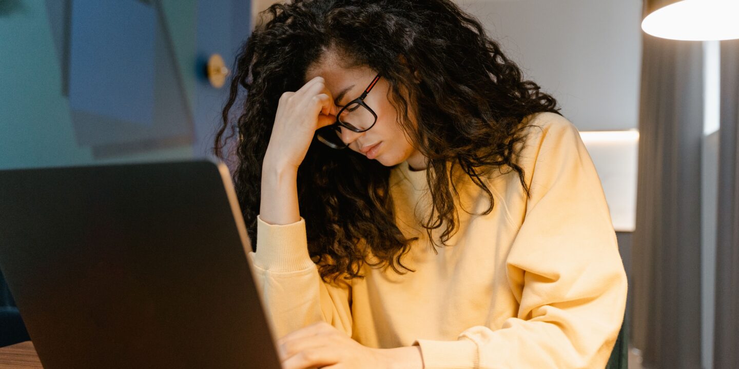 Designer sitting at a laptop with a stressed expression while working late on business tasks.