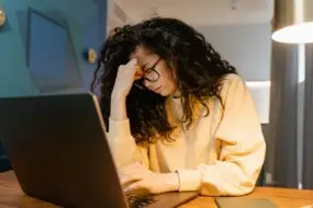 Designer sitting at a laptop with a stressed expression while working late on business tasks.