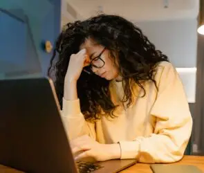 Designer sitting at a laptop with a stressed expression while working late on business tasks.
