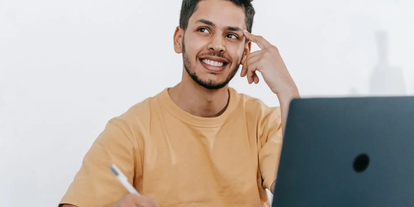 Designer sitting at a laptop while taking notes and thinking through future business plans and objectives.