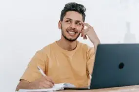 Designer sitting at a laptop while taking notes and thinking through future business plans and objectives.