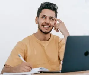 Designer sitting at a laptop while taking notes and thinking through future business plans and objectives.