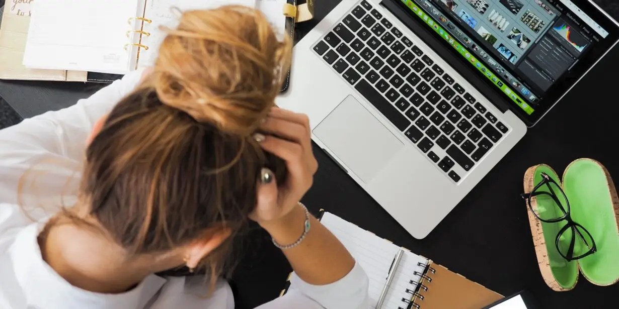 Overwhelmed designer managing multiple projects, schedules, and creative files at a cluttered workspace.