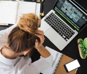 Overwhelmed designer managing multiple projects, schedules, and creative files at a cluttered workspace.
