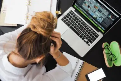 Overwhelmed designer managing multiple projects, schedules, and creative files at a cluttered workspace.
