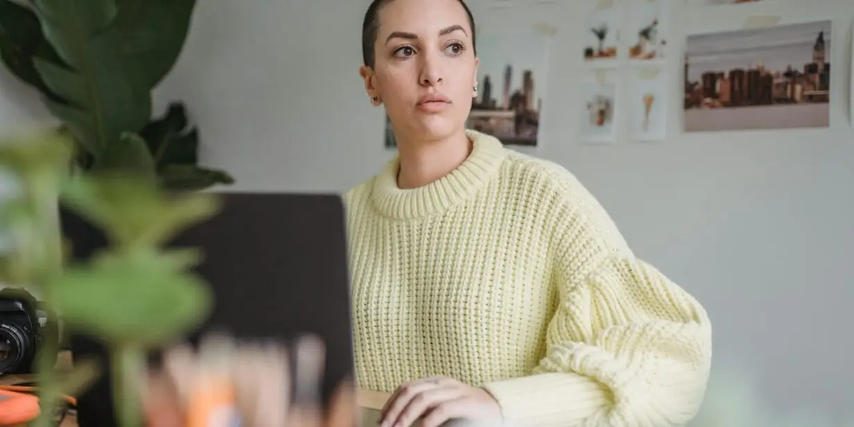 Designer reflecting while working from a laptop in a creative workspace.