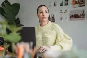 Designer reflecting while working from a laptop in a creative workspace.