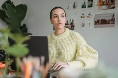 Designer reflecting while working from a laptop in a creative workspace.