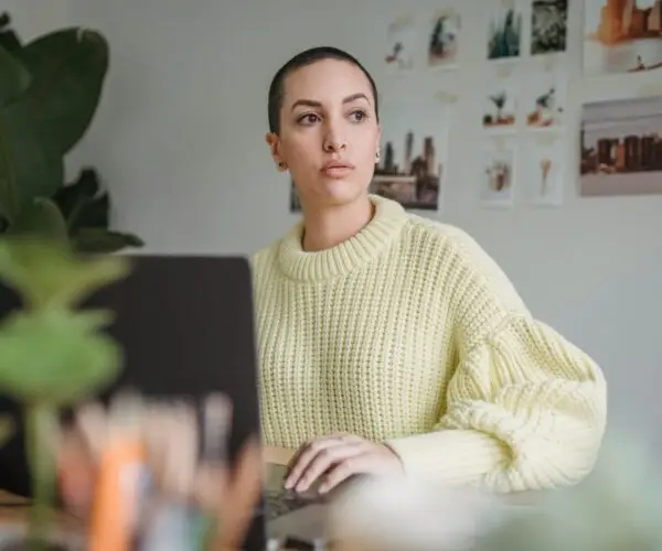Designer reflecting while working from a laptop in a creative workspace.