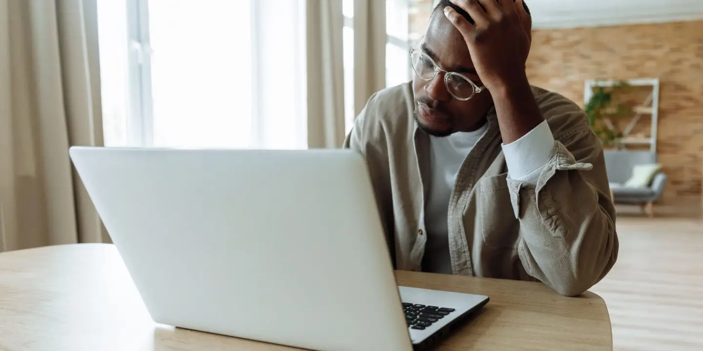 Designer feeling overwhelmed while working on a laptop in a home office.
