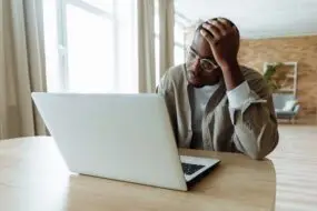 Designer feeling overwhelmed while working on a laptop in a home office.