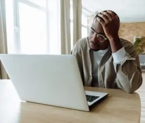 Designer feeling overwhelmed while working on a laptop in a home office.