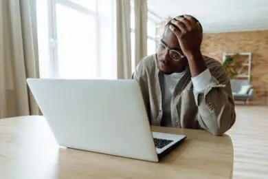 Designer feeling overwhelmed while working on a laptop in a home office.