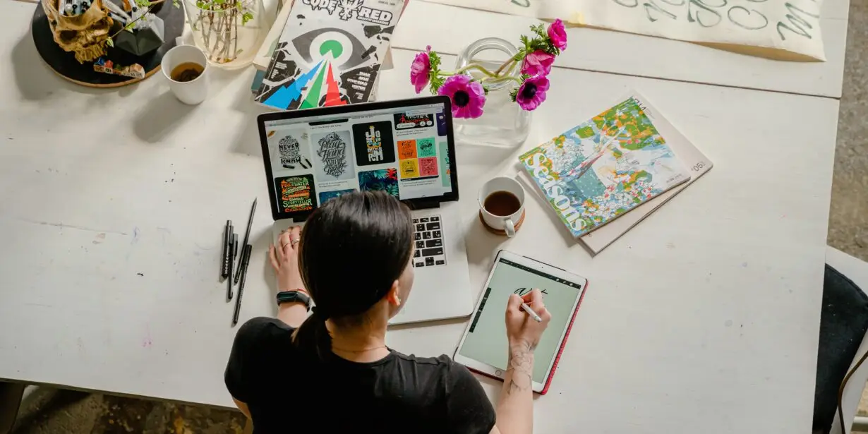 Freelance designer working on a laptop and tablet, developing specialized creative work to grow a design business.