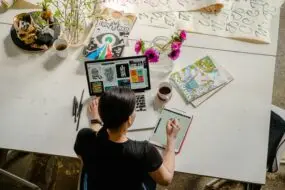 Freelance designer working on a laptop and tablet, developing specialized creative work to grow a design business.