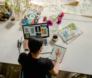 Freelance designer working on a laptop and tablet, developing specialized creative work to grow a design business.